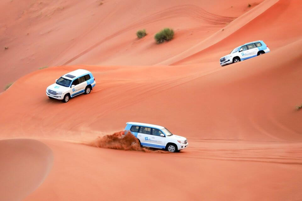 two 4x4 vehicles bashing side to side through the desert dunes in the evening sun Dubai, UAE